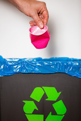 Hand putting single-use plastic cup into recycling bin. Person in a house kitchen separating waste....