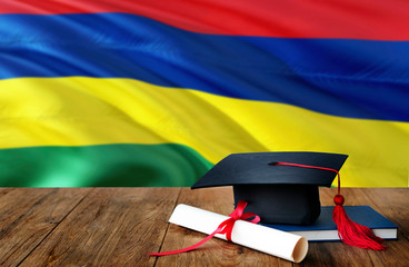 Mauritius education concept. Graduation cap and diploma on wooden table, national flag background....