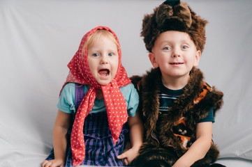 Beautiful couple of lovely children in bear costume and russian cartoon clothes sitting on bed with funny faces. Soft focus portrait of little children in costumes