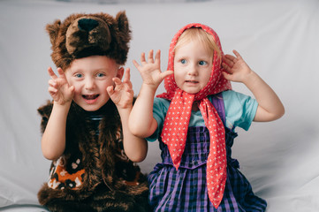 Beautiful couple of lovely children in bear costume and russian cartoon clothes sitting on bed with funny faces. Soft focus portrait of little children in costumes