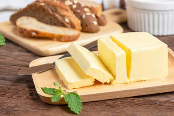 Fresh butter cut with knife on wooden plate and bread.