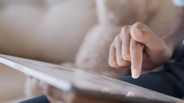 Hand of little girl using  digital tablet to learn while sitting on the sofa in the living room at home