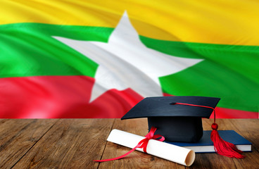 Myanmar education concept. Graduation cap and diploma on wooden table, national flag background....
