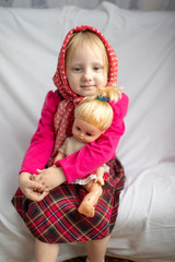 Portrait of lovely little girl sitting on bed with her loving doll