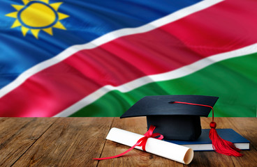 Namibia education concept. Graduation cap and diploma on wooden table, national flag background....
