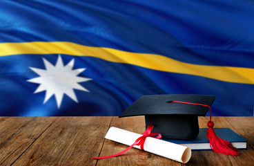 Nauru education concept. Graduation cap and diploma on wooden table, national flag background....