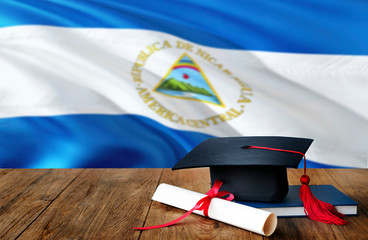 Nicaragua education concept. Graduation cap and diploma on wooden table, national flag background....