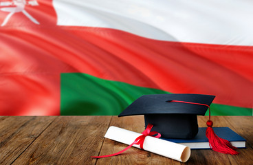 Oman education concept. Graduation cap and diploma on wooden table, national flag background....