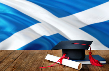 Scotland education concept. Graduation cap and diploma on wooden table, national flag background....