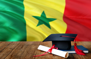 Senegal education concept. Graduation cap and diploma on wooden table, national flag background. Succesful student.