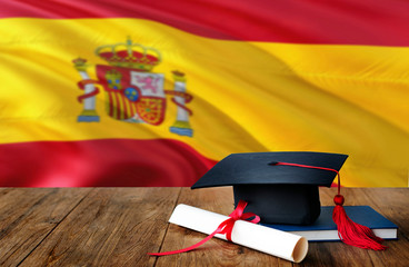 Spain education concept. Graduation cap and diploma on wooden table, national flag background....