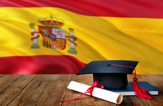 Spain education concept. Graduation cap and diploma on wooden table, national flag background. Succesful student.