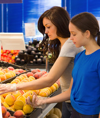 Teen girl with mother shopping in the supermarket at the fruit section. Choosing daily product. Concept of healthy food, bio, vegetarian, diet.