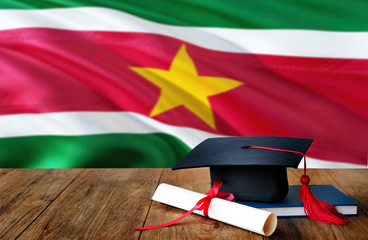 Suriname education concept. Graduation cap and diploma on wooden table, national flag background. Succesful student.