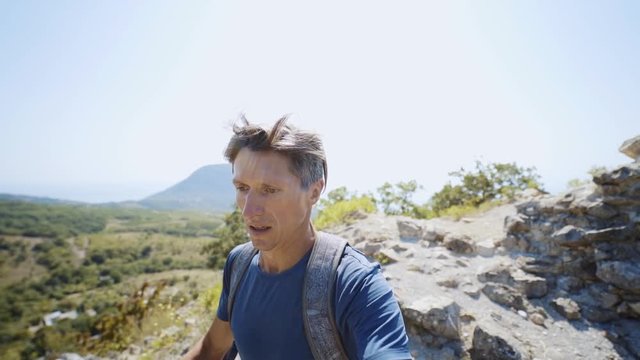 closeup wide angle slow motion selfie portrait of young adult man trail runner running on mountain ridge at summer day. guy runs fast, hair flutters, frequently breathing, tense face