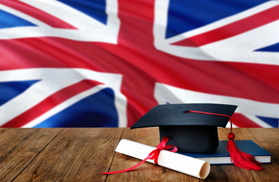 United Kingdom education concept. Graduation cap and diploma on wooden table, national flag background. Succesful student.