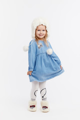 Smiling little surprised girl in a blue dress and a winter white fur hat having fun on White isolated background