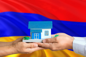 Armenia real estate concept. Man and woman holding miniature house in hands. Citizenship theme and national flag on background.