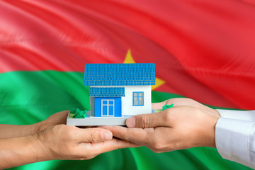 Burkina Faso real estate concept. Man and woman holding miniature house in hands. Citizenship theme and national flag on background.