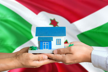 Burundi real estate concept. Man and woman holding miniature house in hands. Citizenship theme and national flag on background.