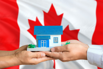 Canada real estate concept. Man and woman holding miniature house in hands. Citizenship theme and...