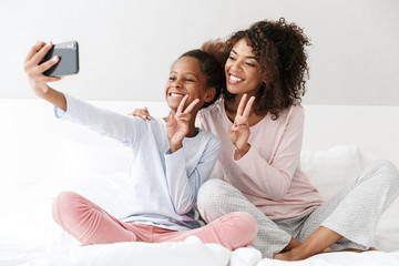 Image of american woman and little daughter taking selfie at home