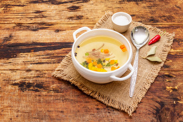 Transparent duck broth in bowl with vegetables. Traditional bouillon, healthy meal. Old wooden background