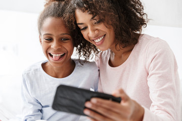 Image of american woman and little daughter taking selfie at home