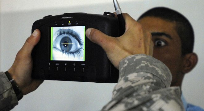 An Iraqi police recruit holds his eye open for a retinal scan administered by a US Soldier in Mahmudiyah Iraq May 30 2007