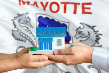 Mayotte real estate concept. Man and woman holding miniature house in hands. Citizenship theme and national flag on background.