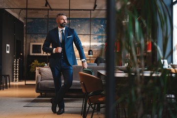 Stylish bearded man in a suit standing in modern office - obrazy, fototapety, plakaty