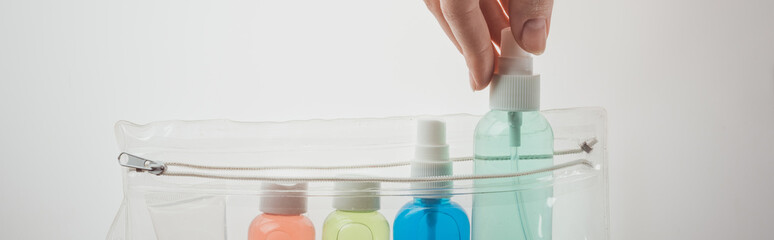 panoramic shot of woman putting bottle with liquid to cosmetic bag on white background