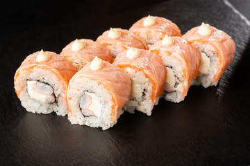 Sushi Rolls with flamed salmon, shrimp, crab meat and Cream Cheese inside on black slate isolated. Philadelphia roll sushi with shrimp. Sushi menu. Horizontal photo.
