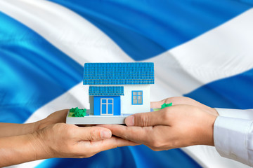 Scotland real estate concept. Man and woman holding miniature house in hands. Citizenship theme and national flag on background.