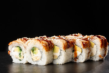 Sushi Rolls with cucumber, avocado, eel, omelet and Cream Cheese inside on black slate isolated. Philadelphia unagi roll sushi with tamago. Sushi menu. Horizontal photo.