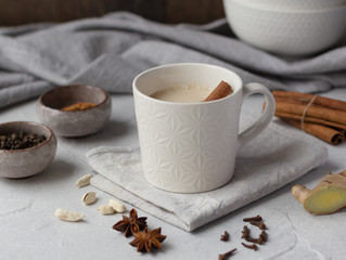 Indian masala chai, traditional spiced  black tea with milk in white cup and spice ingredients on...