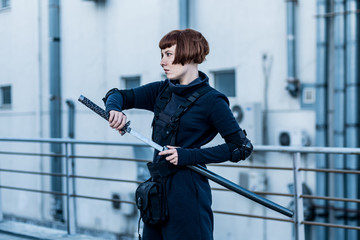 portrait of young redhead woman with japanese sword dressed in futuristic cyberpunk costume standing on the roof. 