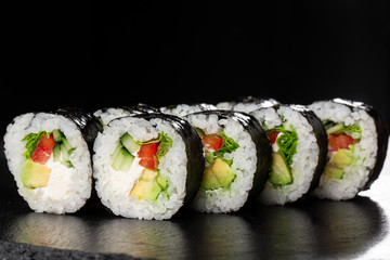 Sushi Rolls with salade, avocado, cucumber, pepper and Cream Cheese inside. Maki Futomaki Sushi Rolls with salmon on black background. Sushi menu. Japanese food. Horizontal photo.