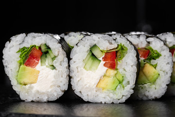 Sushi Rolls with salade, avocado, cucumber, pepper and Cream Cheese inside. Maki Futomaki Sushi Rolls with salmon on black background. Sushi menu. Japanese food. Horizontal photo.