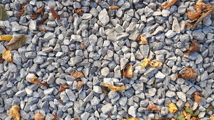 small road stone background, dark gravel pebbles stone texture with golden and yellow leaves in autumn season