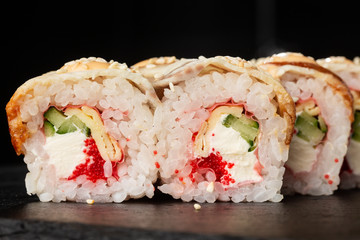 Sushi Rolls with cucumber, flying fish caviar, eel, omelet and Cream Cheese inside on black slate isolated. Philadelphia unagi roll sushi with tamago. Sushi menu. Horizontal photo.