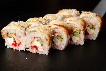 Sushi Rolls with cucumber, flying fish caviar, eel, omelet and Cream Cheese inside on black slate isolated. Philadelphia unagi roll sushi with tamago. Sushi menu. Horizontal photo.