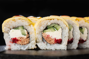 Sushi Rolls with cucumber, cheddar, flying fish caviar , tuna and Cream Cheese inside on black slate isolated. Philadelphia cheddar roll sushi with tuna. Sushi menu. Horizontal photo.