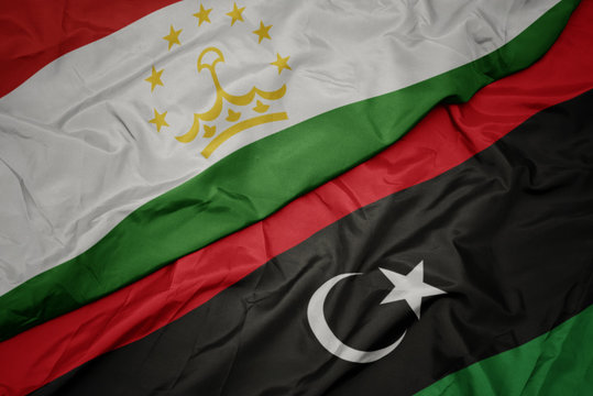 waving colorful flag of libya and national flag of tajikistan.