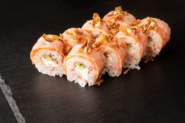 Sushi Rolls with cucumber, shrimp, crab meat, flamed salmon and Cream Cheese inside and fried onion on top on black slate isolated. Philadelphia roll sushi with flamed salmon . Sushi menu. Horizontal