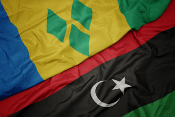 waving colorful flag of libya and national flag of saint vincent and the grenadines.
