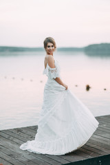 Fototapeta na wymiar Wedding dress in European style. Happy bride at sunset on the lake.
