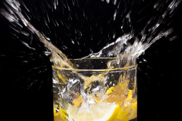 Limón entrando en un vaso o jarro de cristal transparente lleno de agua, chapoteo, agua salpicando y saliendo del vaso