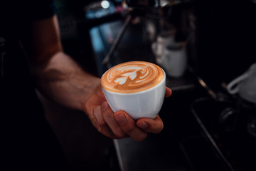 Close up of barista hands showing cup of cappuccino in coffee shop. - obrazy, fototapety, plakaty