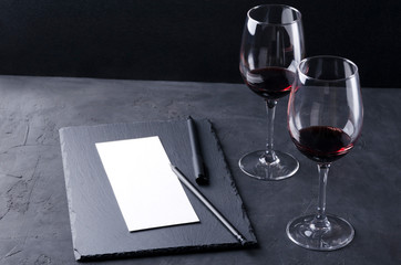 Wine tasting process. Empty degustation card for notes, several wine glasses on the dark surface